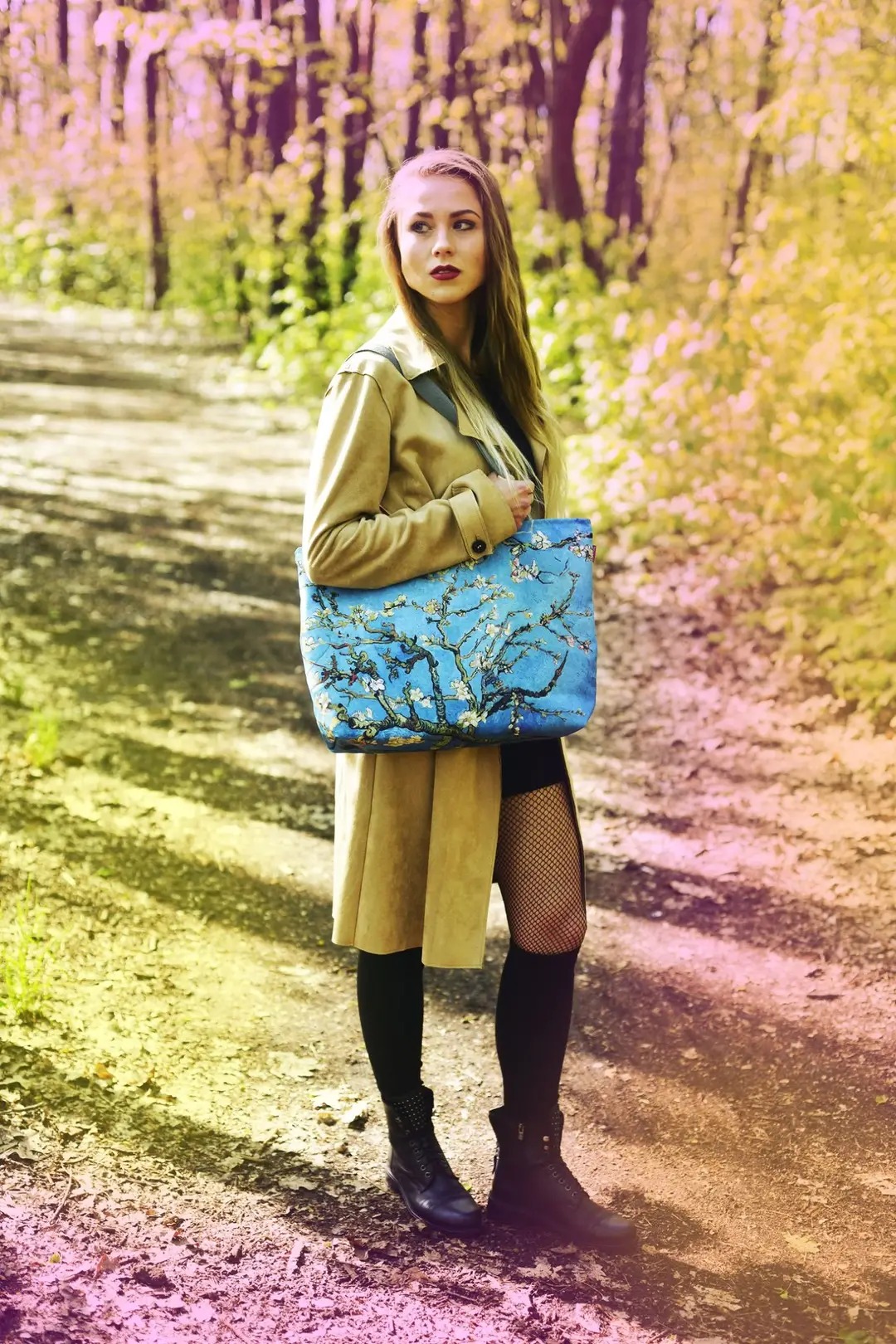 Kobieta w płaszczu i z torbą z motywem kwitnących migdałowców na spacerze po Pabianicach, w tle leśna ścieżka.