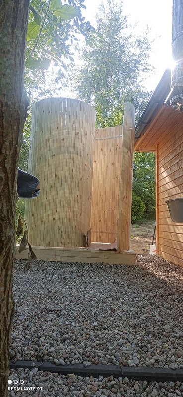 Drewniana sauna beczka w trakcie budowy, widoczna z zewnątrz, z elementami konstrukcyjnymi i otoczeniem naturalnym. Częściowo zmontowana konstrukcja.