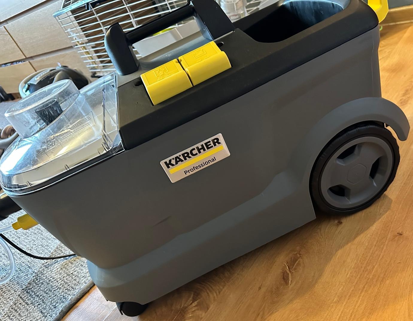 Profesjonalny odkurzacz piorący marki Karcher, widoczny zbiornik na wodę i naklejka z logo, stoi na drewnianej podłodze.