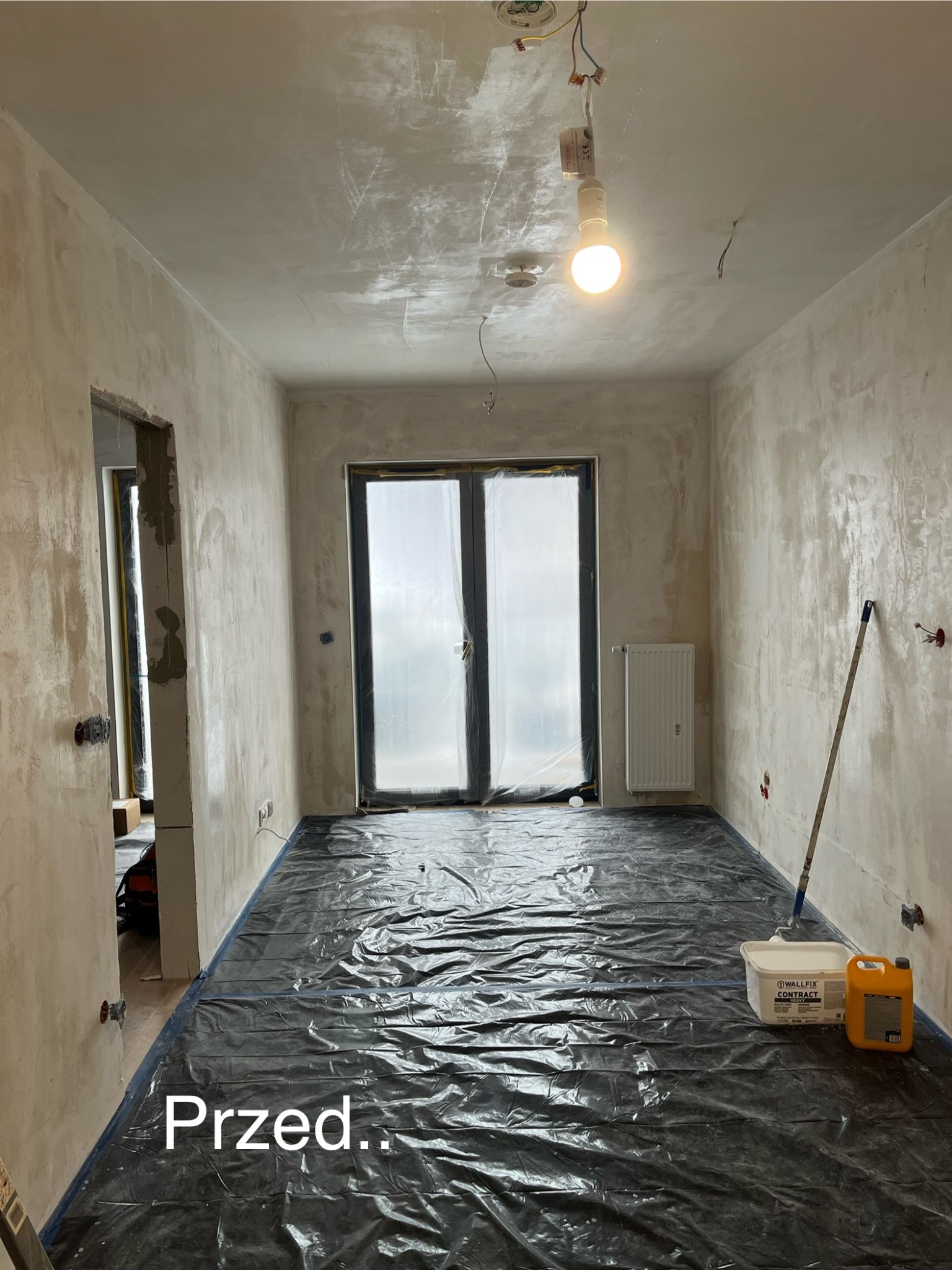 Przygotowanie do prac wykończeniowych w Jeleniej Górze: pokój zabezpieczony folią malarską, ściany wstępnie przygotowane, widoczny grunt i wiadro z masą szpachlową.