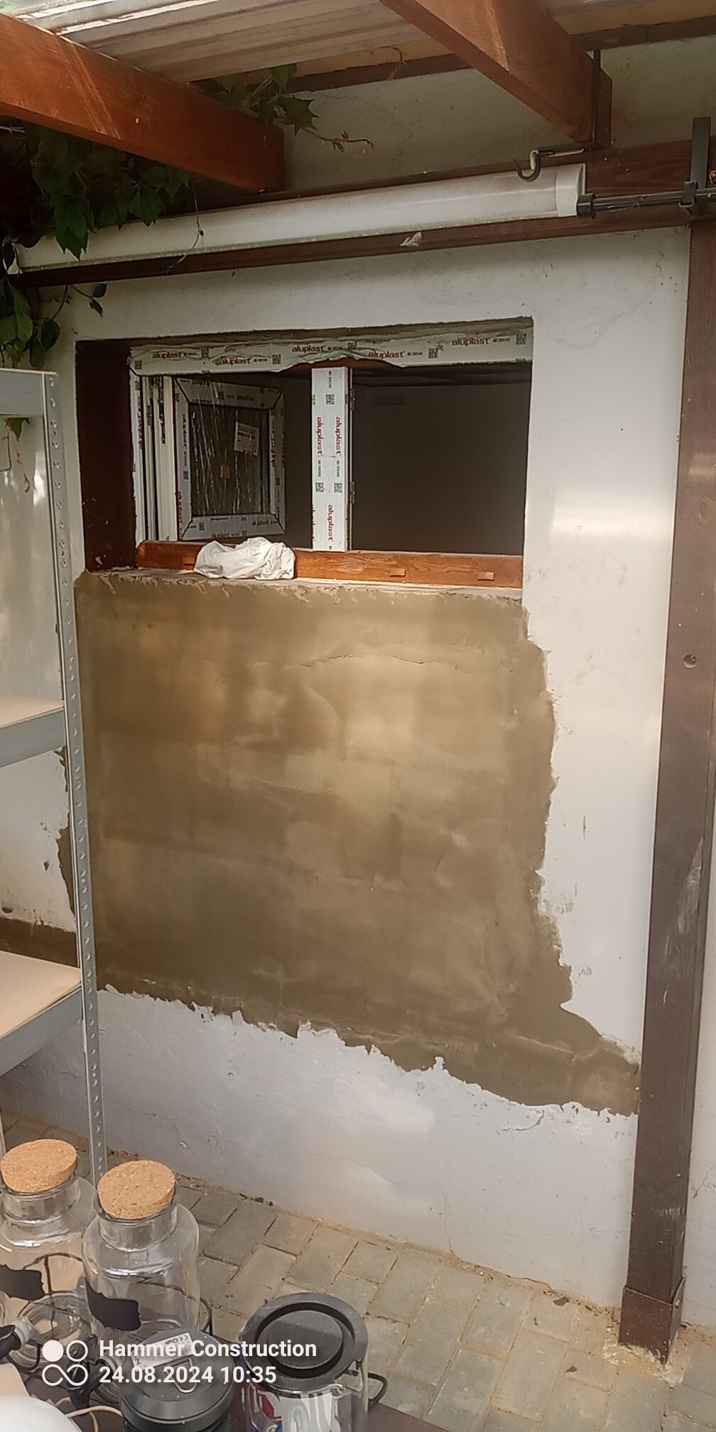 Ściana z częściowo nałożoną warstwą szpachli w pomieszczeniu z oknem, widoczne przygotowania do dalszych prac wykończeniowych.