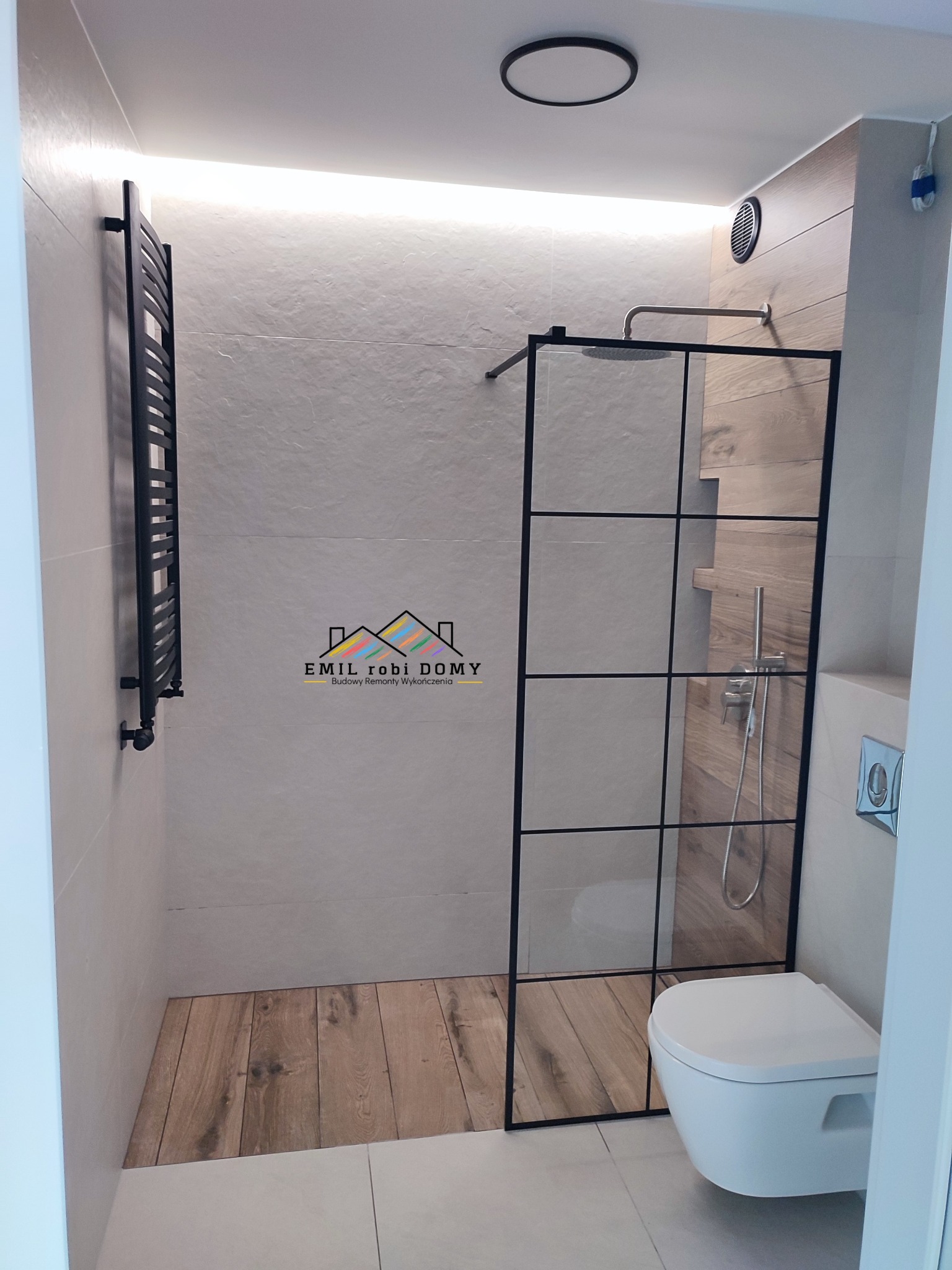 Nowoczesna łazienka z kabiną prysznicową typu walk-in z czarną ramą, drewnopodobnymi płytkami na ścianie prysznica i drewnianą podłogą w strefie prysznicowej, grzejnik drabinkowy w kolorze czarnym,...