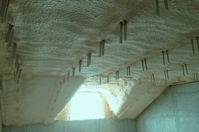 Poddasze po ociepleniu pianką poliuretanową, widoczne metalowe elementy mocujące wystające z piany, okno w ścianie szczytowej.