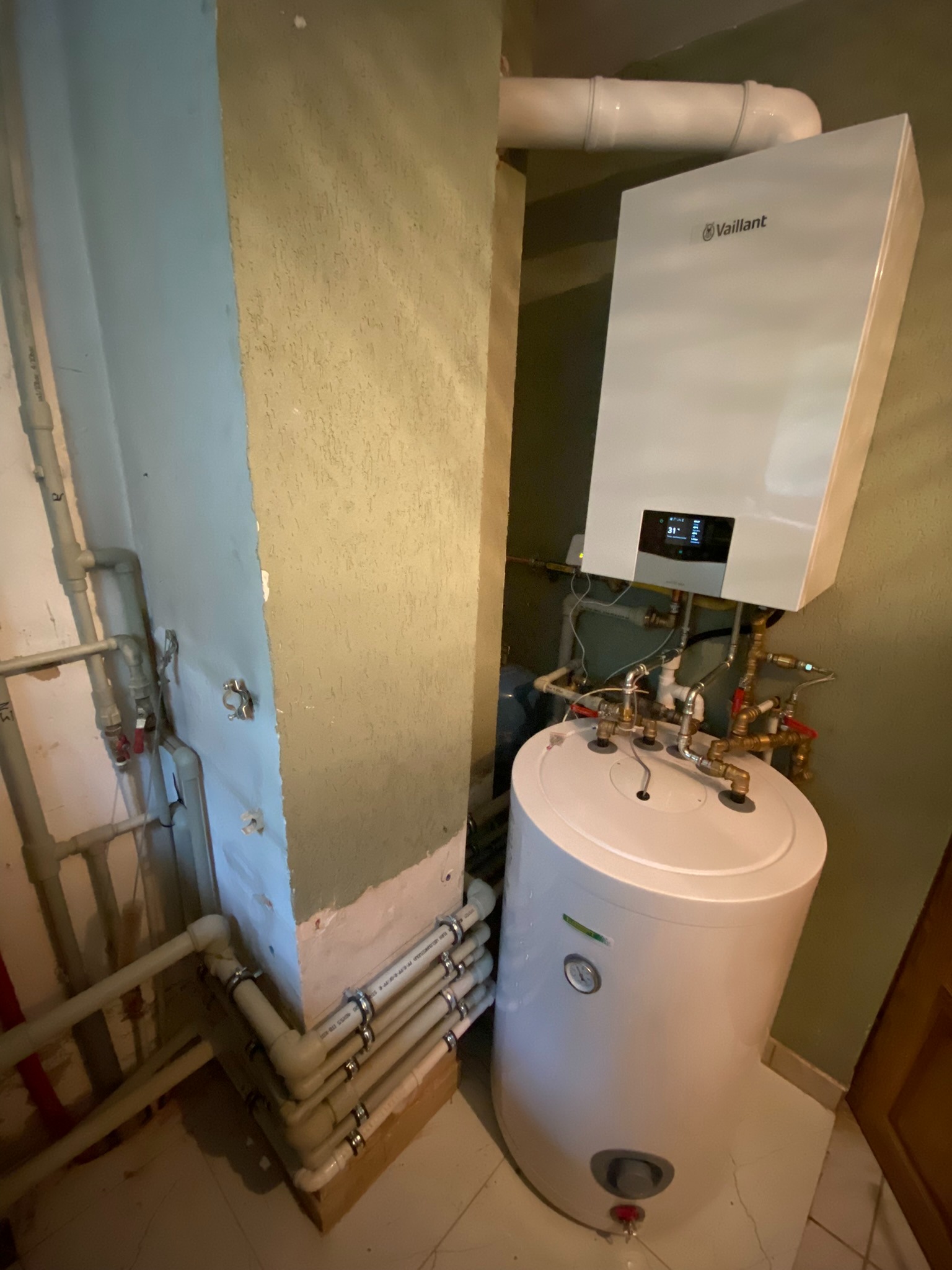 Zainstalowany gazowy kocioł kondensacyjny Vaillant z podgrzewaczem wody, widoczne rury instalacyjne i przyłącza, zamontowane w pomieszczeniu o nierównych ścianach.