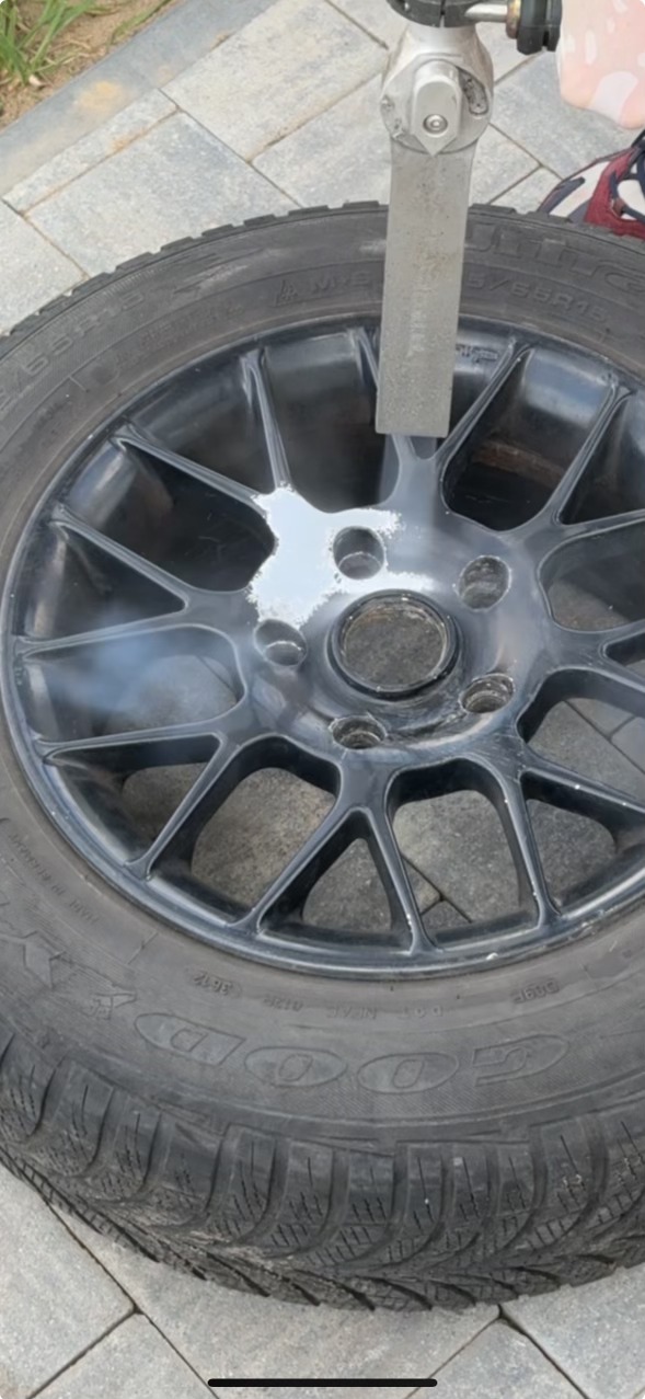 Częściowo oczyszczona felga samochodowa z oponą, przy użyciu narzędzia do obróbki strumieniowo-ściernej, widoczne ślady po procesie czyszczenia.