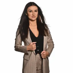 Kobieta w beżowym garniturze w prążki i czarnej kamizelce, prezentująca się jako doradca finansowy w Toruniu, z delikatnym uśmiechem i rozwianymi włosami.