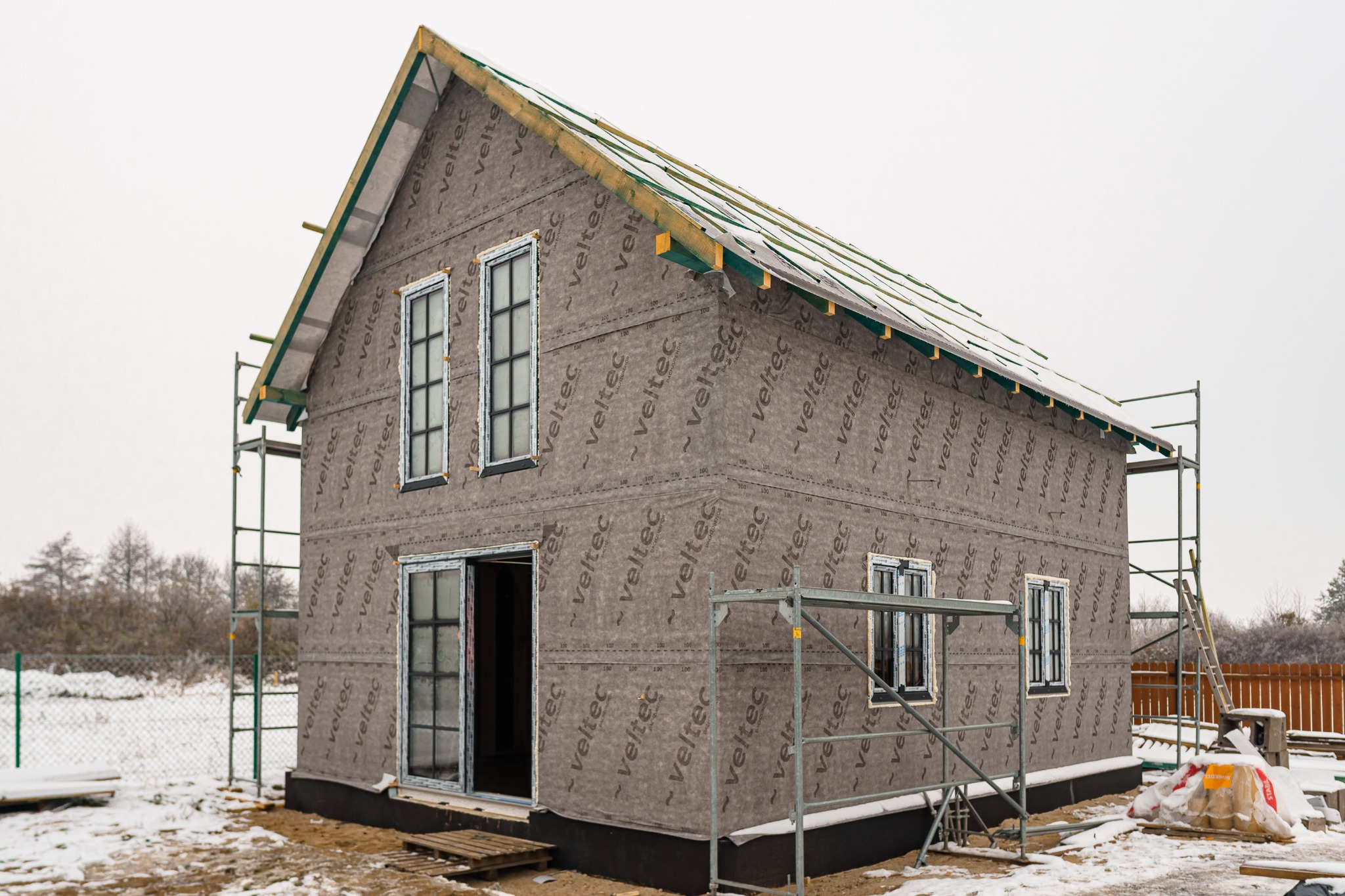 Niedokończony budynek z widoczną membraną elewacyjną Veltec, osadzony w zimowym krajobrazie, z rusztowaniami i częściowo ośnieżonym dachem.