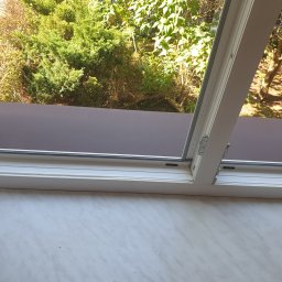 Czarodziejka - Otwarty fragment okna z widokiem na zieleń na zewnątrz, widoczny parapet wewnętrzny z wzorem marmurkowym.