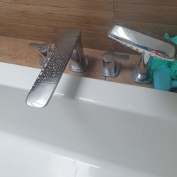 Czarodziejka - Bateria wannowa z chromowanym wykończeniem pokryta kroplami wody, obok leży zielona myjka i niebieska zabawka do kąpieli, widoczne ślady czyszczenia na białej powierzchni wanny.