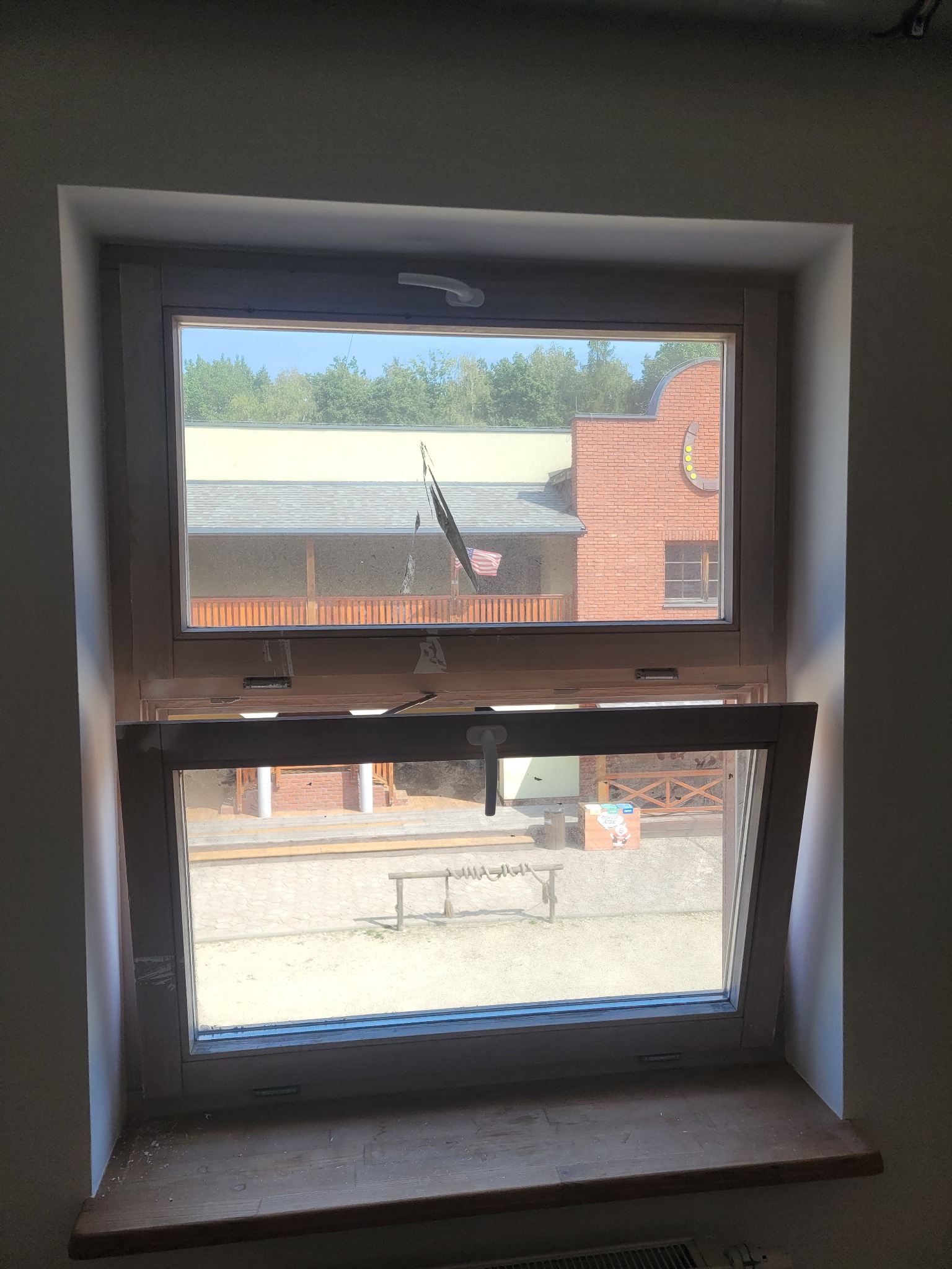 Drewniane okno z widokiem na miasteczko westernowe, dolna część okna uchylona, widoczne zabrudzenia na parapecie.