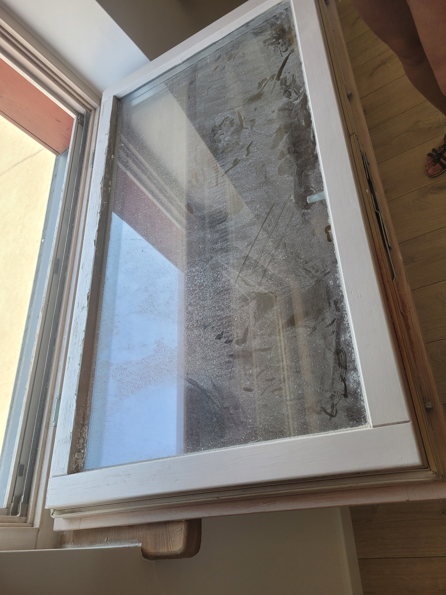 Otwarty, brudny okno z drewnianą ramą przed czyszczeniem, widoczne zacieki i osad na szybie.