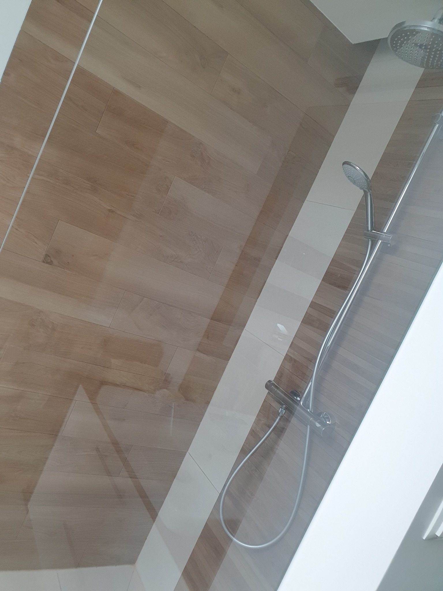 Szklana kabina prysznicowa z drewnopodobnymi płytkami ściennymi i chromowaną armaturą.