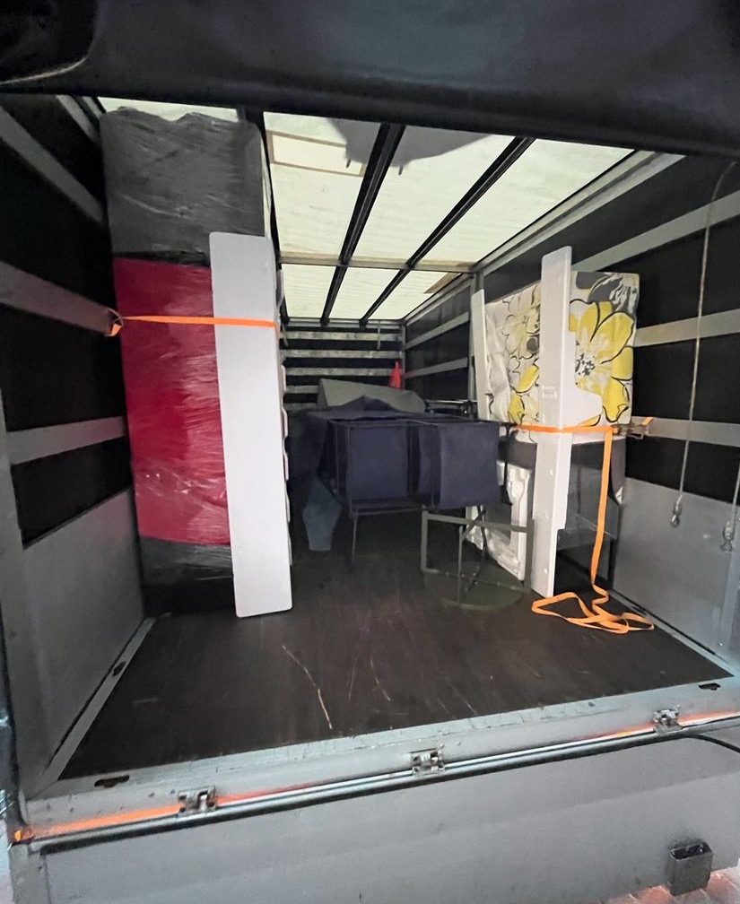 Wnętrze furgonetki załadowane meblami zabezpieczonymi pasami transportowymi: zapakowane w folię krzesła, stół i inne elementy wyposażenia wnętrz.