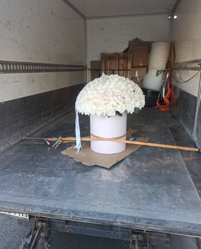 Karton z bukietem białych róż zabezpieczony wewnątrz skrzyni ładunkowej podczas transportu.