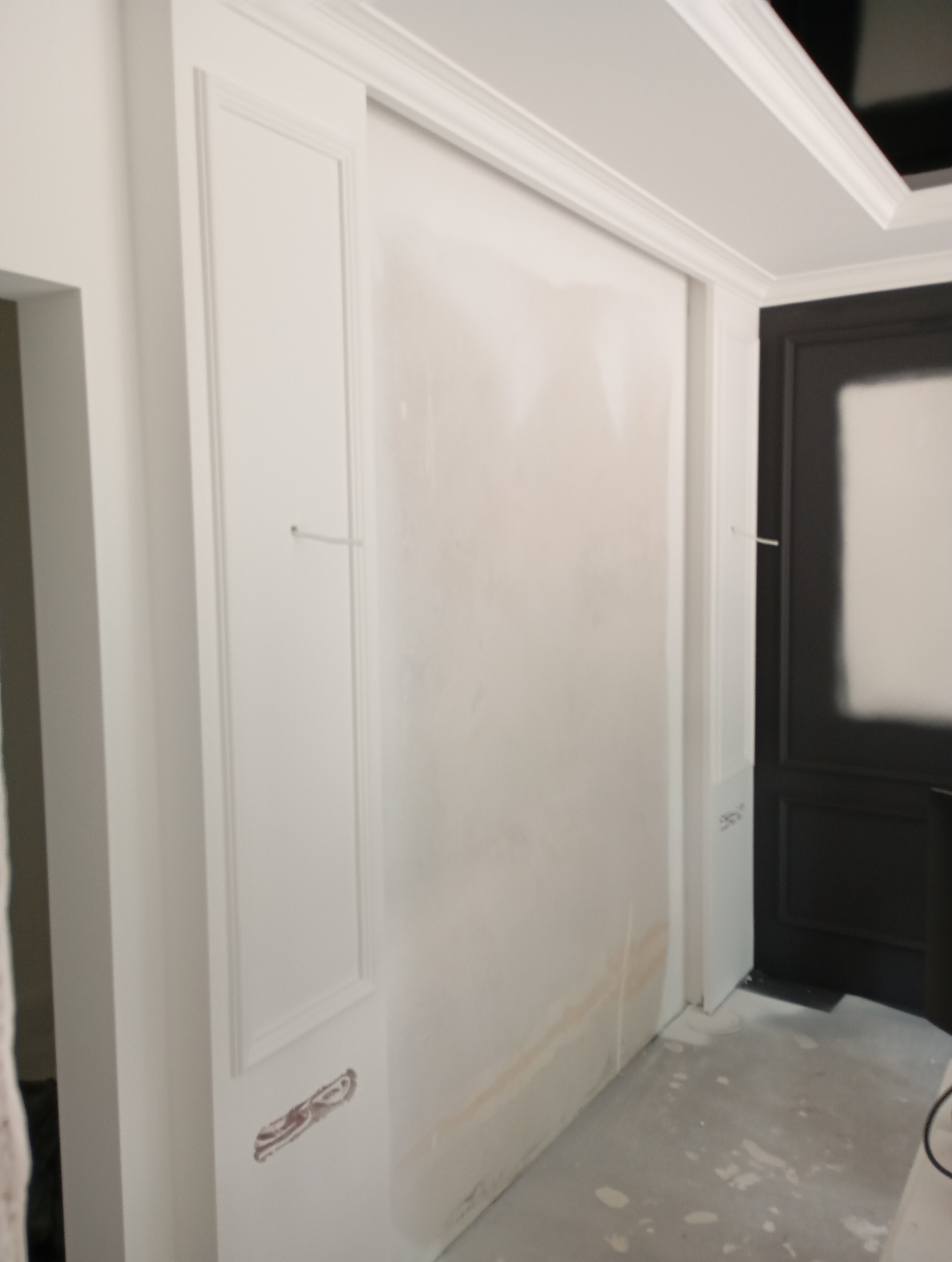 Ściana po szpachlowaniu z widocznymi śladami po łatach, przygotowana do malowania, z dekoracyjnymi listwami przy suficie i wzdłuż ściany.