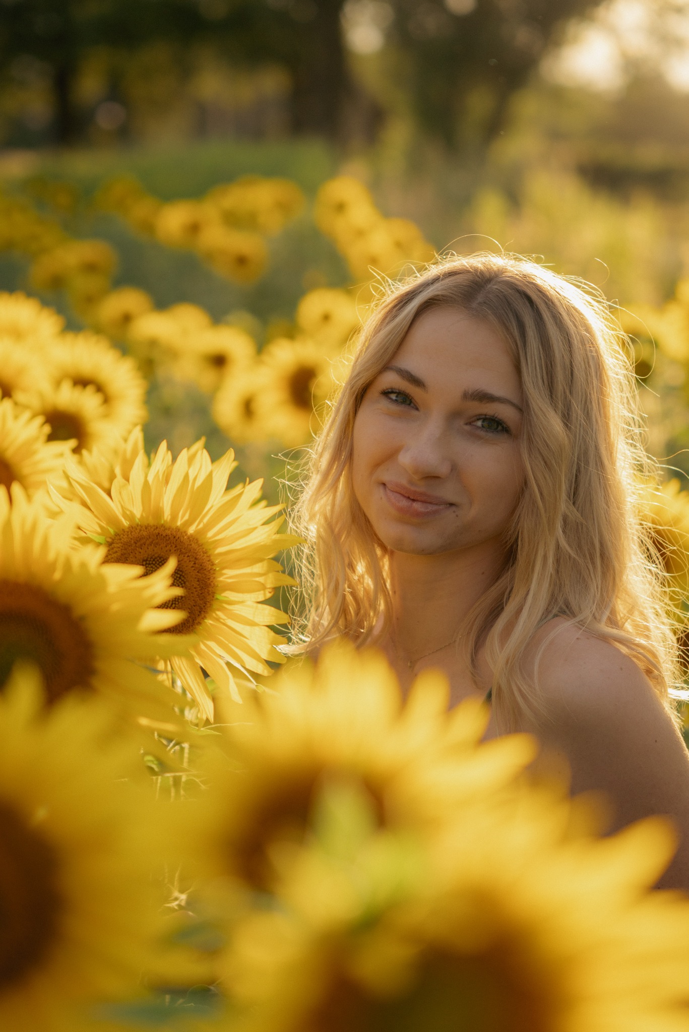 Uśmiechnięta blondynka w polu słoneczników, delikatne światło zachodzącego słońca, miękkie tło z rozmytych kwiatów.
