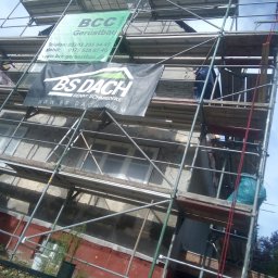 Evry-Bud - Budynek w trakcie prac elewacyjnych, widoczne rusztowania z reklamami firm, pracownik na rusztowaniu, oraz fragmenty starej i nowej elewacji.