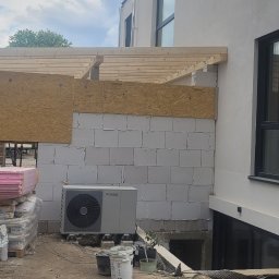 Evry-Bud - Budowa zadaszenia nad tarasem w Szczecinie, widoczne białe bloczki, drewniana konstrukcja dachu, płyty OSB, materiały budowlane i pompa ciepła.