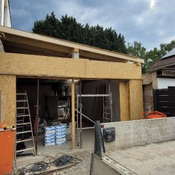 Evry-Bud - Budowa rozbudowy domu w trakcie: drewniane elementy konstrukcyjne, płyty OSB, rusztowania, drabina i zapas materiałów budowlanych widoczne na placu budowy.