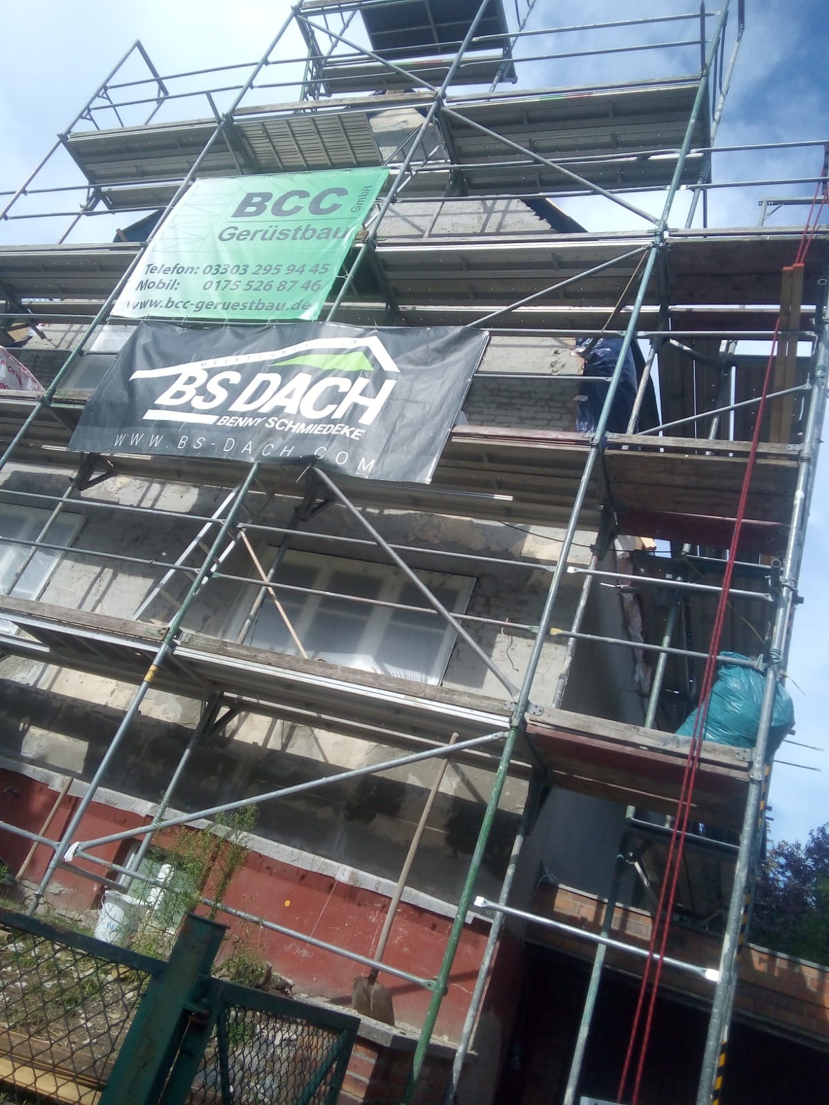 Budynek w trakcie prac elewacyjnych, widoczne rusztowania z reklamami firm, pracownik na rusztowaniu, oraz fragmenty starej i nowej elewacji.