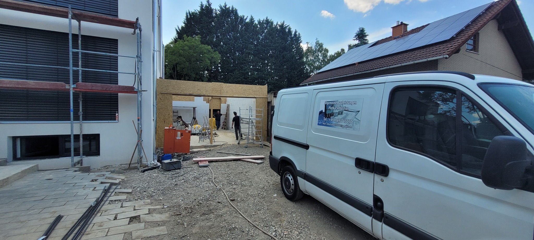 Budowa domu w trakcie realizacji: widoczna konstrukcja z płyt OSB, rusztowania przy ścianie, gruz na podłożu i samochód dostawczy z reklamą firmy budowlanej.