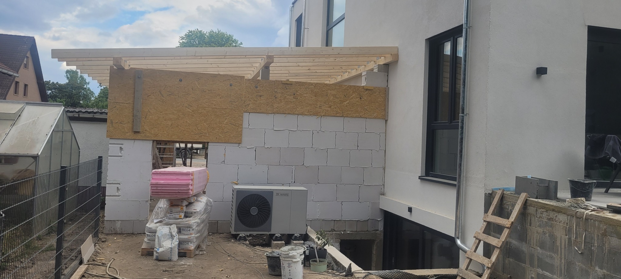 Budowa zadaszenia nad tarasem w Szczecinie, widoczne białe bloczki, drewniana konstrukcja dachu, płyty OSB, materiały budowlane i pompa ciepła.