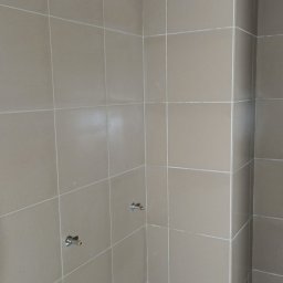 WOJT-KRAZ - Ściana łazienki wyłożona beżowymi płytkami ceramicznymi, widoczne dwa wystające zawory wodne, ściana w trakcie prac wykończeniowych, góra ściany jeszcze nie wykończona.