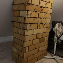 WOJT-KRAZ - Wznoszenie konstrukcji z cegieł na poddaszu, z użyciem krzyżyków dystansowych, widoczny wentylator i skośny sufit.