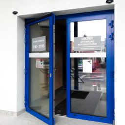 ALU-HOUSE Brzycki - Automatyczne drzwi wejściowe z niebieską ramą, częściowo otwarte, z widocznym napisem 'Godziny otwarcia' i informacją o obowiązku noszenia maseczki, zamontowane w Ropczycach.