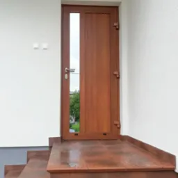 Drewniane drzwi wejściowe z szybą, zamontowane na zewnątrz budynku z białymi ścianami i brązowymi schodami z płytek.