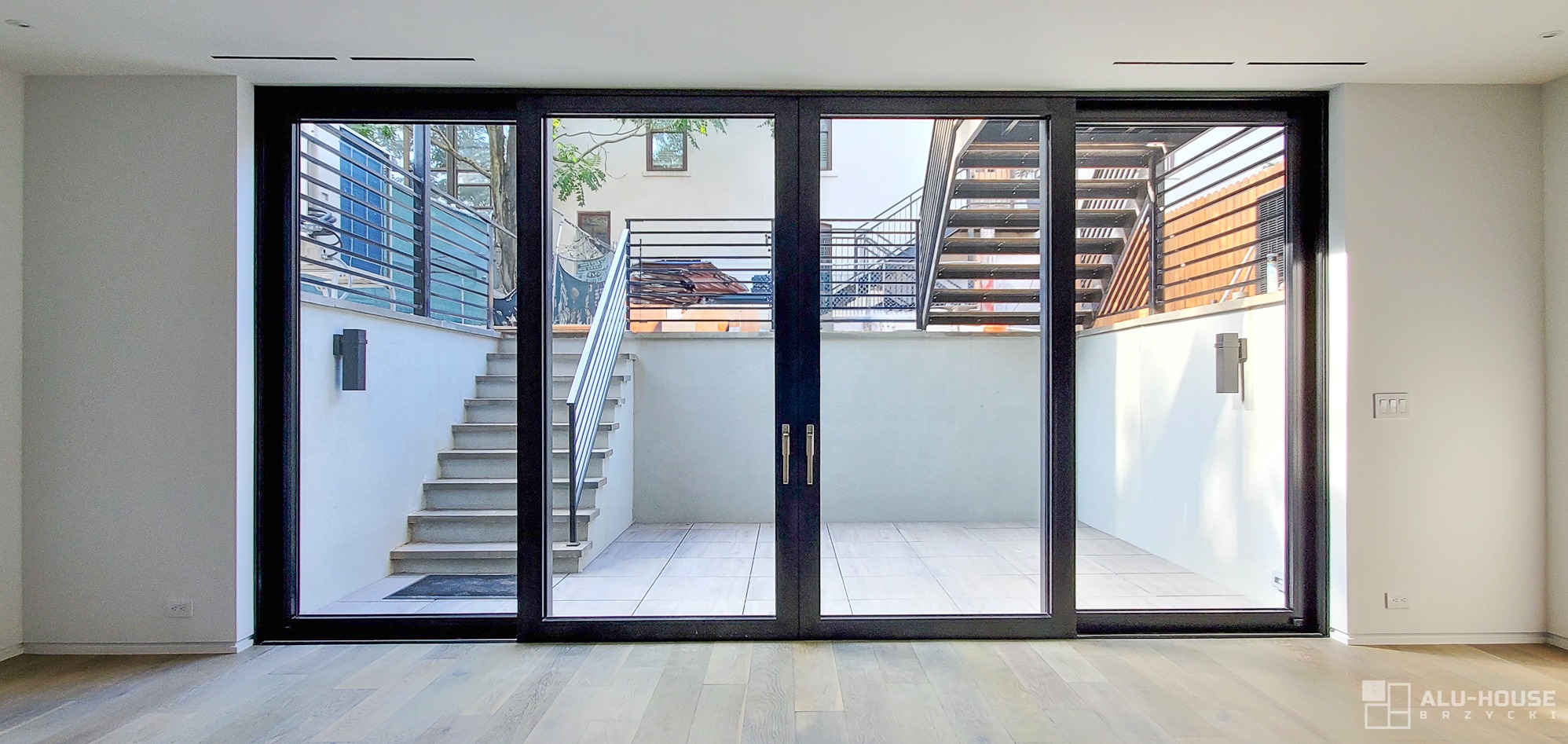 Nowoczesne, czarne, przesuwne drzwi szklane z widokiem na patio z zewnętrznymi schodami i metalowymi balustradami.