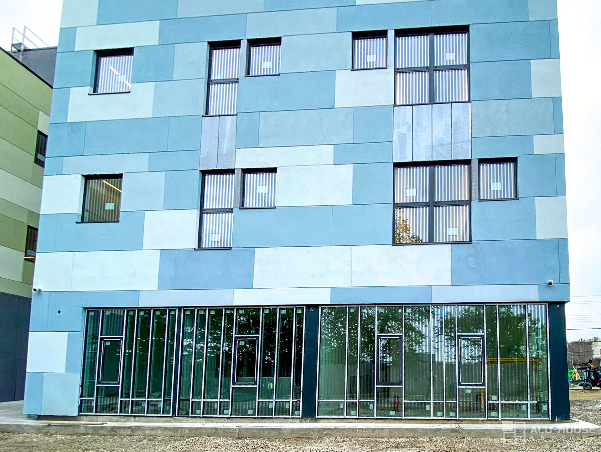 Fasada budynku biurowego z oknami i przeszklonym parterem, niebiesko-szara kolorystyka elewacji.