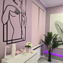 Wow-Body - Nowoczesny gabinet kosmetyczny w odcieniach fioletu z minimalistyczną dekoracją ścienną przedstawiającą kobiecą sylwetkę, sztuczną palmą i białymi meblami.