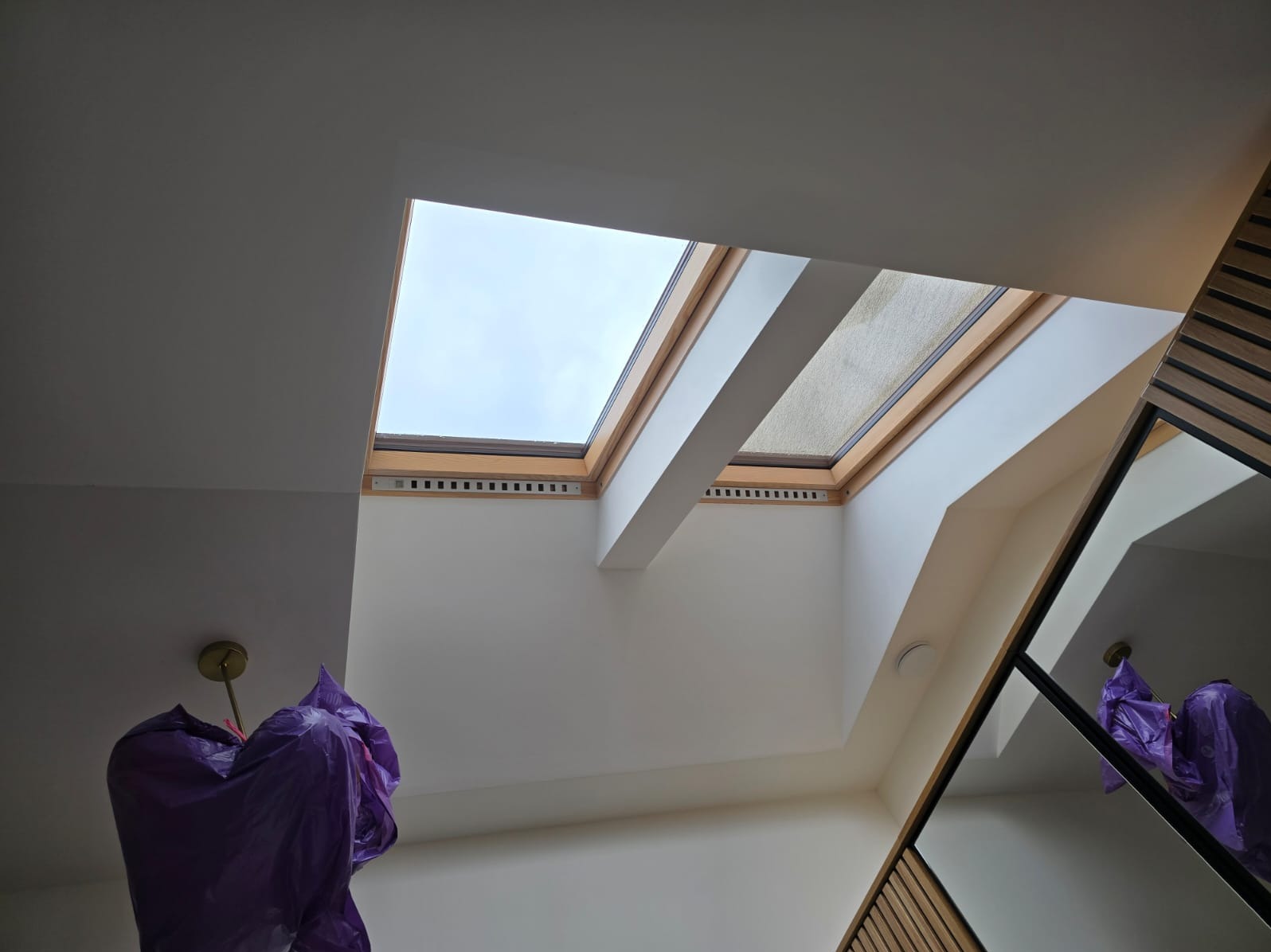 Wnętrze z widokiem na okno dachowe, z fragmentem lampy zabezpieczonej folią malarską, widoczne drewniane elementy wykończeniowe.