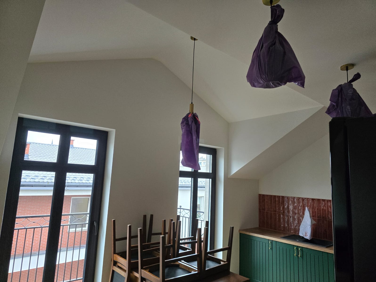 Pokój na poddaszu w trakcie przygotowań do prac malarskich: lampy zabezpieczone folią, krzesła ustawione na stole, ściany świeżo pomalowane na biało.