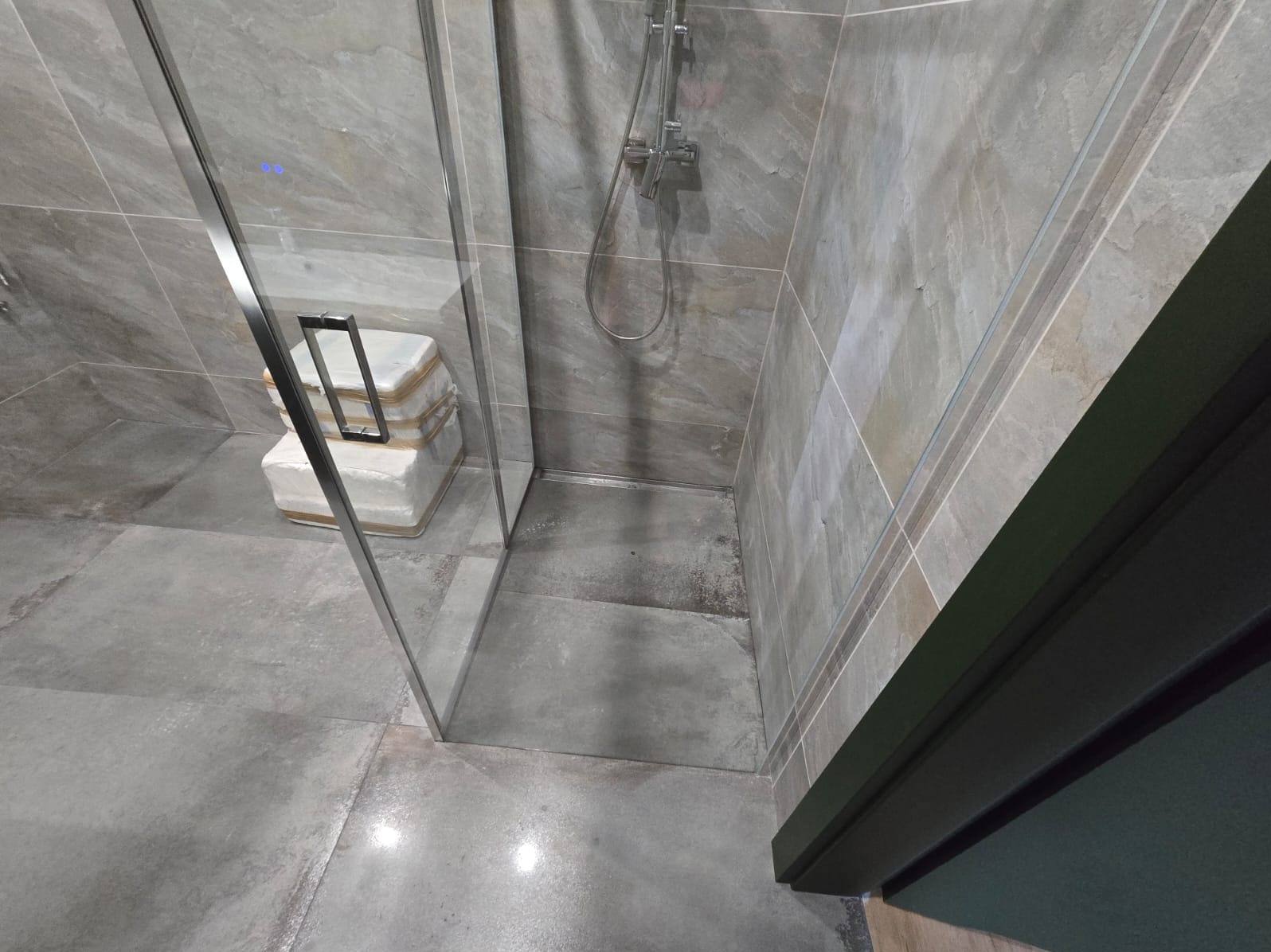 Niedokończona łazienka z szarą, kamienną okładziną, kabiną prysznicową ze srebrnymi okuciami i zapakowanymi płytkami w rogu.
