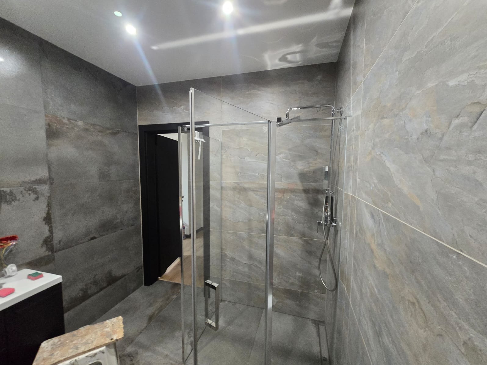 Szklana kabina prysznicowa z deszczownicą, zamontowana w łazience wykończonej płytkami imitującymi kamień w Radomsku.