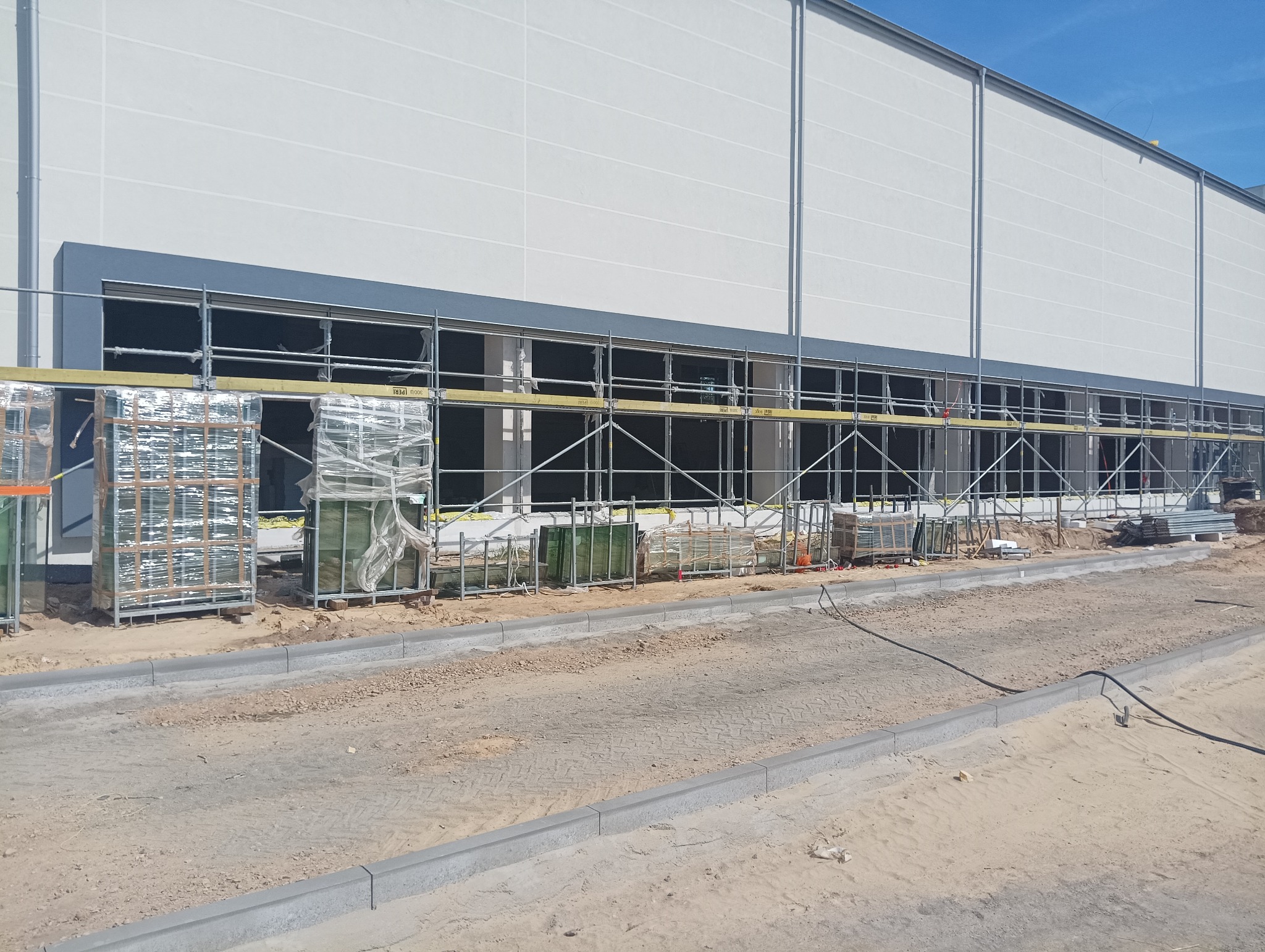 Budynek przemysłowy w trakcie prac elewacyjnych, widoczne rusztowania i materiały budowlane, przygotowane do montażu okna.