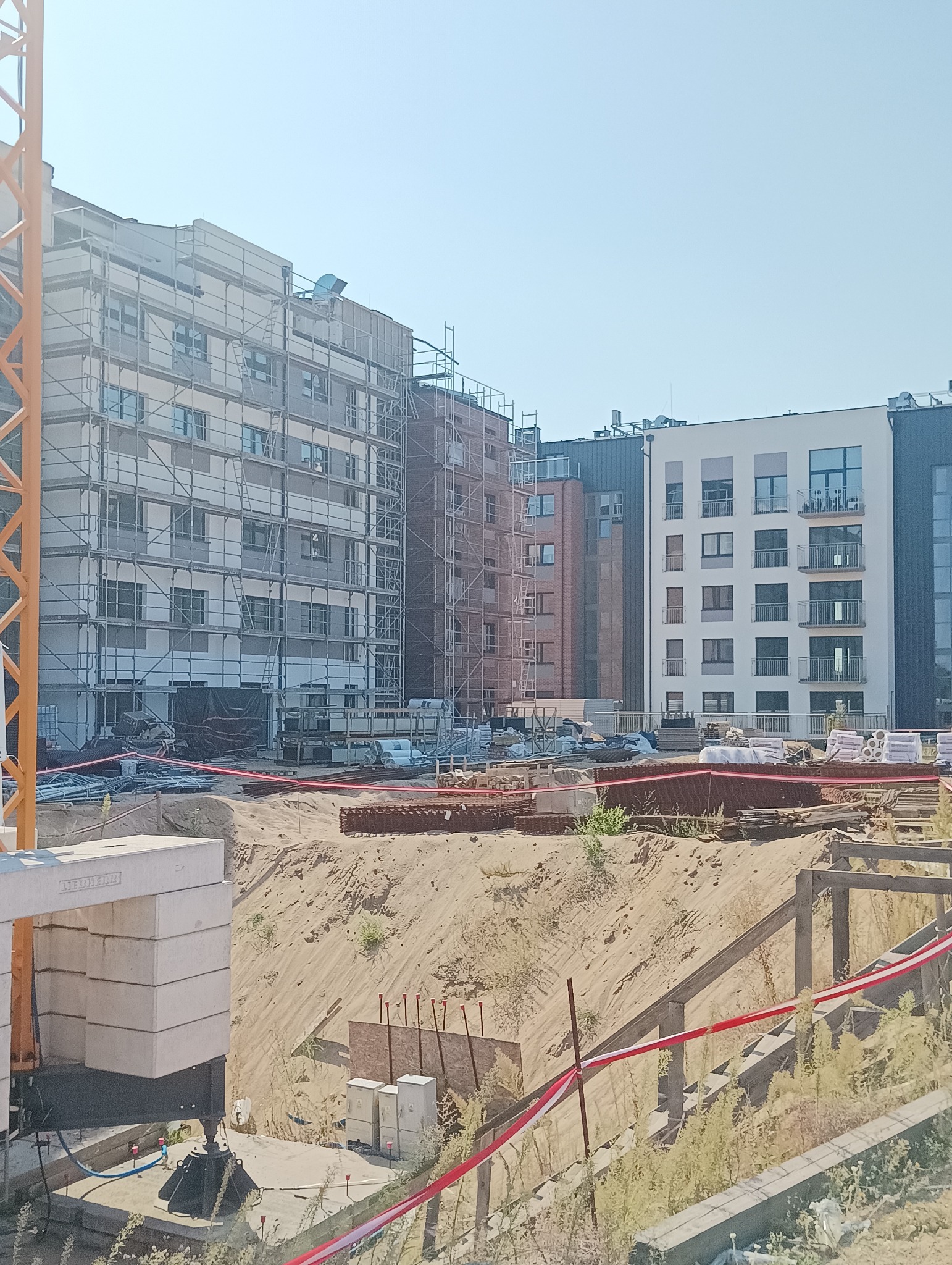 Budynek w trakcie budowy z rusztowaniami, widoczny żuraw i materiały budowlane na placu budowy.