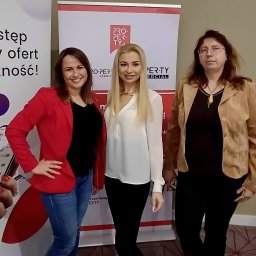 Małgorzata Korólczyk-Rabek - Trzy kobiety stojące na tle baneru reklamowego 'Property' z logo, ubrane w różne style: czerwona marynarka i jeansy, biała bluzka i czarne spodnie, brązowa kurtka i czarne spodnie.