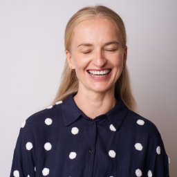 Marek Bąk - Portret roześmianej blondynki z zamkniętymi oczami, ubrana w granatową koszulę w białe kropki.