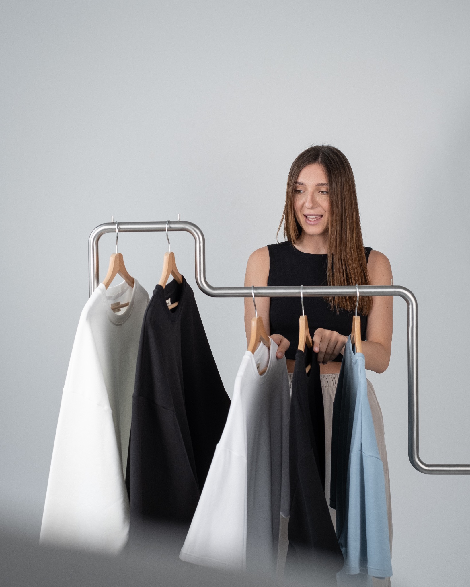 Kobieta przegląda kolekcję ubrań na wieszaku, analizując kolory i fasony bluz.