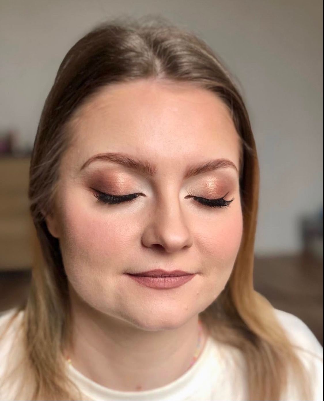 Portret kobiety z zamkniętymi oczami prezentujący makijaż w odcieniach brązu, z wyraźnie podkreślonymi rzęsami i ustami w kolorze nude. Subtelny, dzienny look.