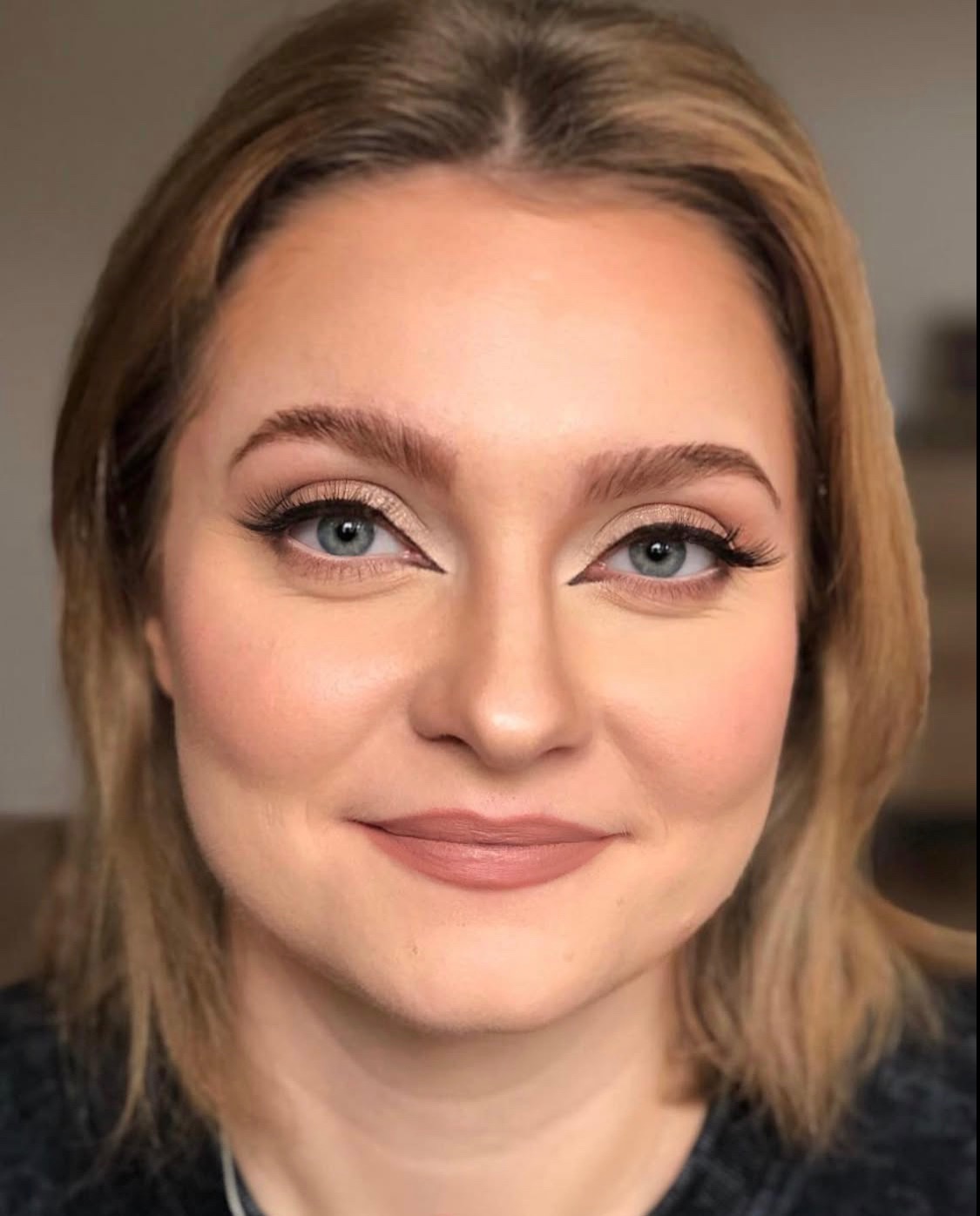 Portret kobiety z profesjonalnym makijażem: beżowe cienie, delikatny róż na policzkach, matowa pomadka w odcieniu nude, podkreślone brwi i sztuczne rzęsy.