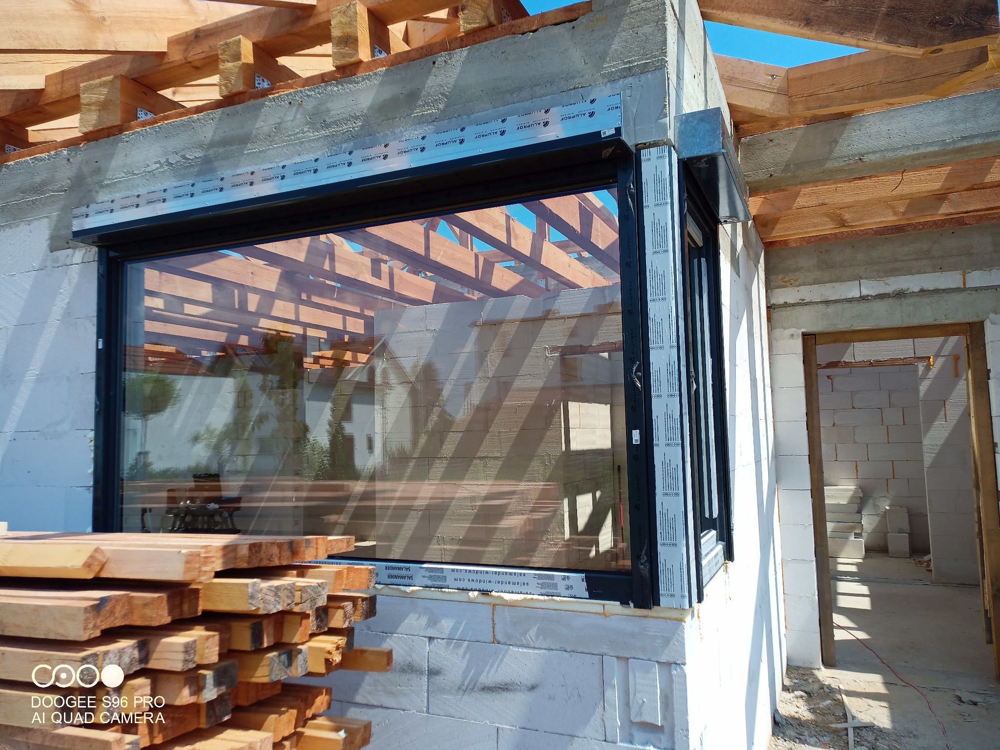 Montaż okna z roletą zewnętrzną w surowym stanie budynku; widoczne materiały budowlane, surowe drewno konstrukcyjne i niezabezpieczone otwory okienne.