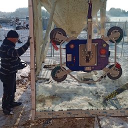 LASERVICE SPÓŁKA Z OGRANICZONĄ ODPOWIEDZIALNOŚCIĄ - Montera okienny z przyssawką Schmalz EasyMaster przenosi duże okno Veka na tle zimowego krajobrazu i betonowego silosu. Widoczne ślady w śniegu.