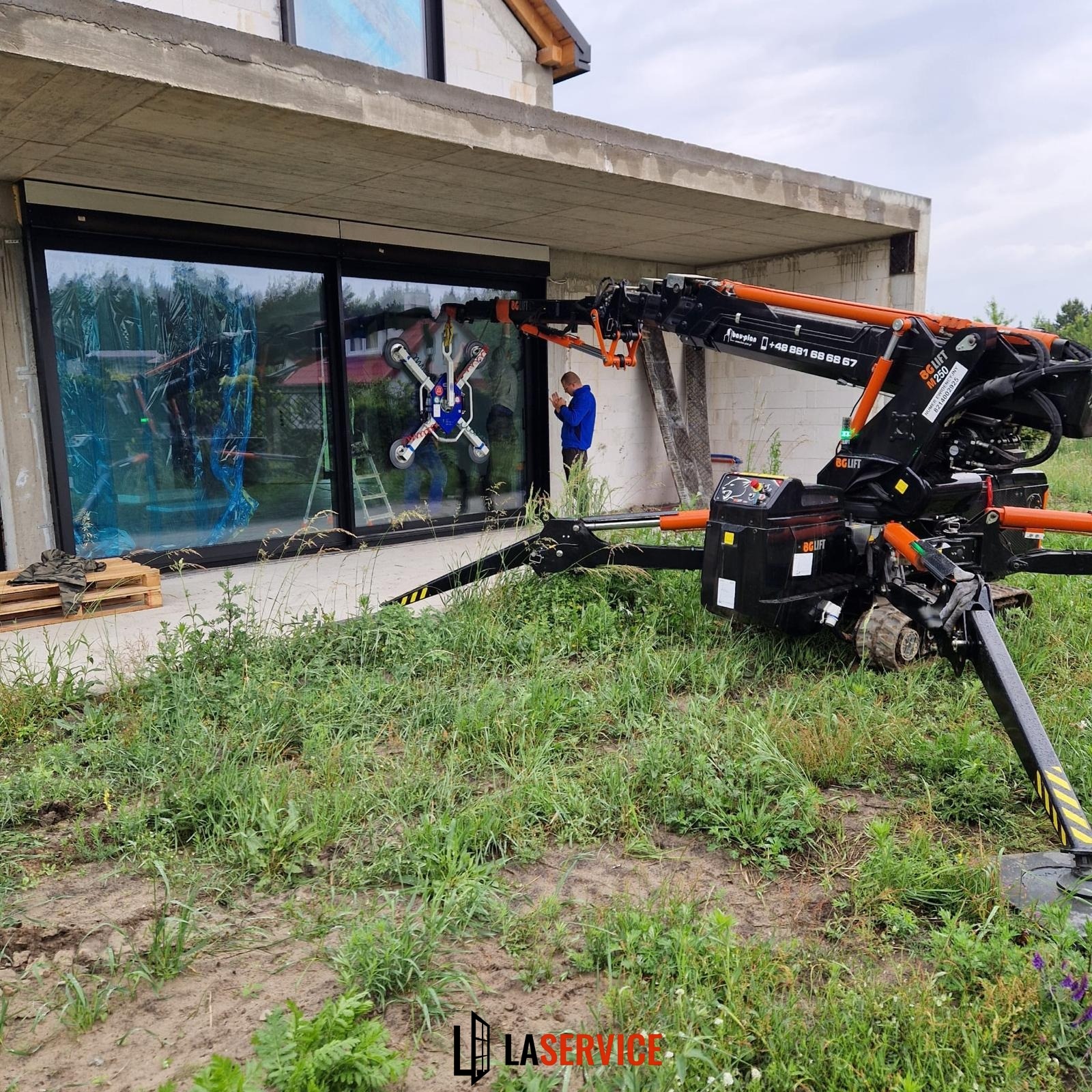 Montaż okna za pomocą specjalistycznego dźwigu przyssawkowego na budowie. Nowoczesne okno z czarną ramą, przymocowane przyssawkami.