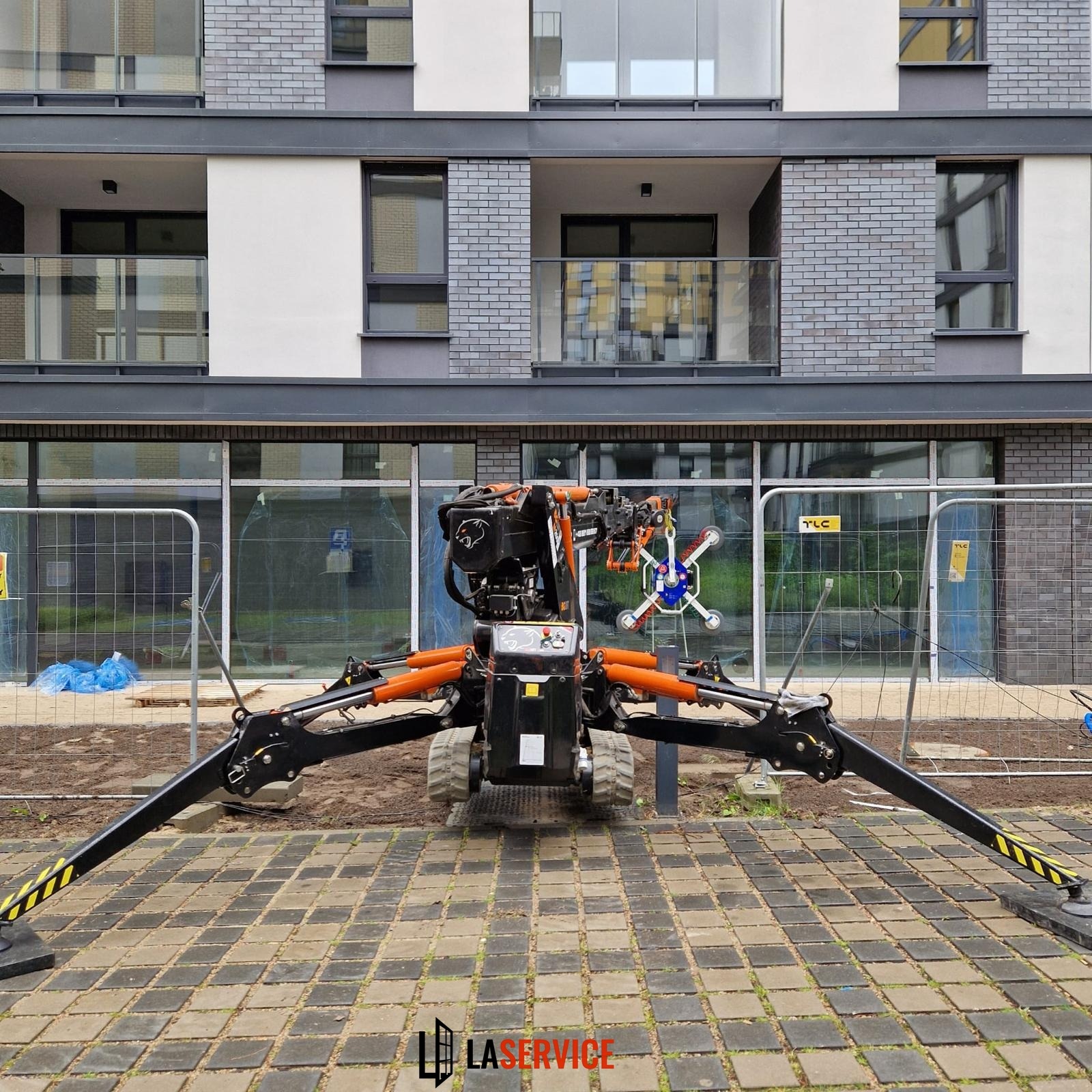 Mini żuraw z przyssawkami do szkła na tle budynku z zamontowanymi oknami. Widoczne zabezpieczenia budowy.