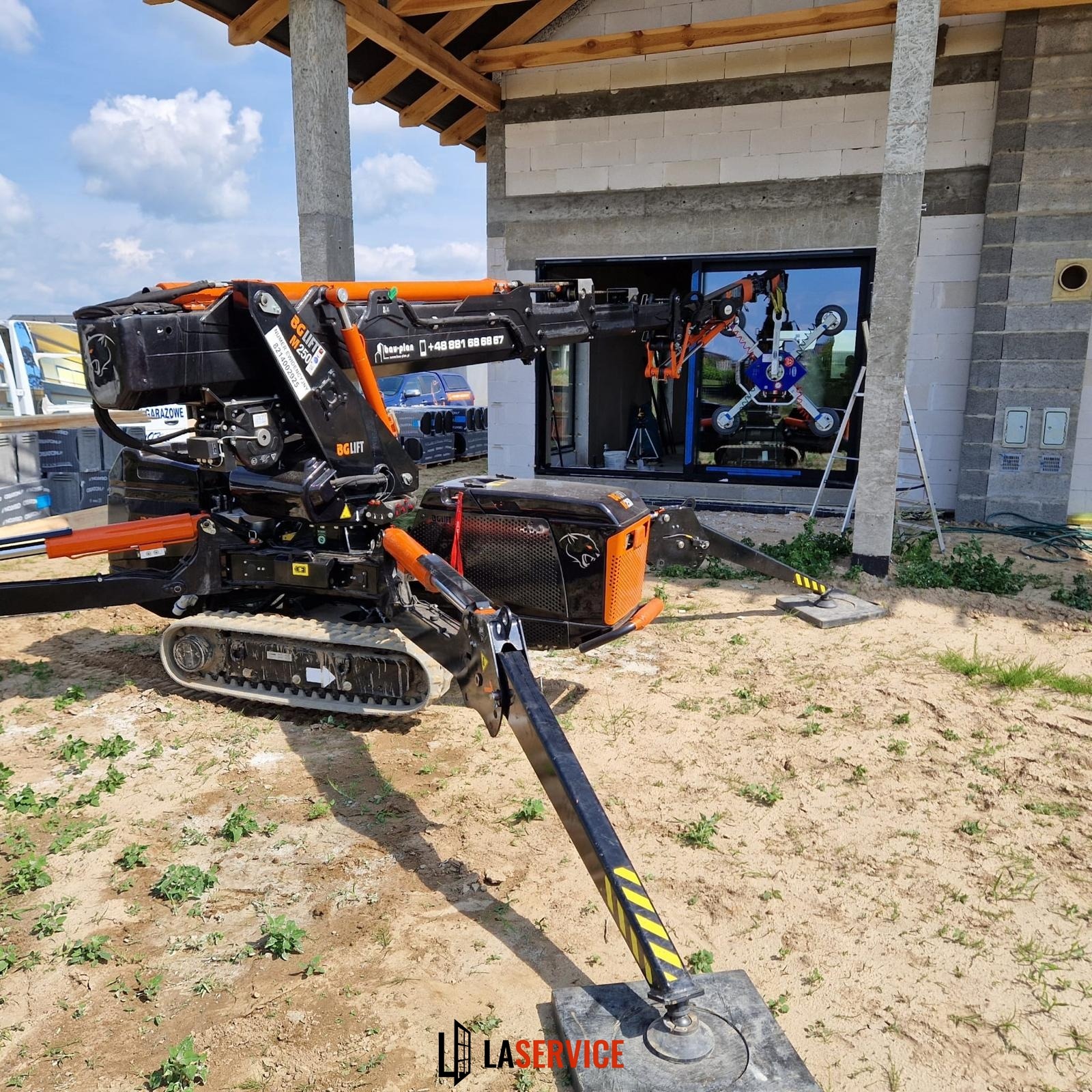 Ciężki sprzęt z przyssawkami montuje szybę w oknie budynku w trakcie budowy. Widoczny dźwig z przyssawkami i elementy konstrukcyjne domu.