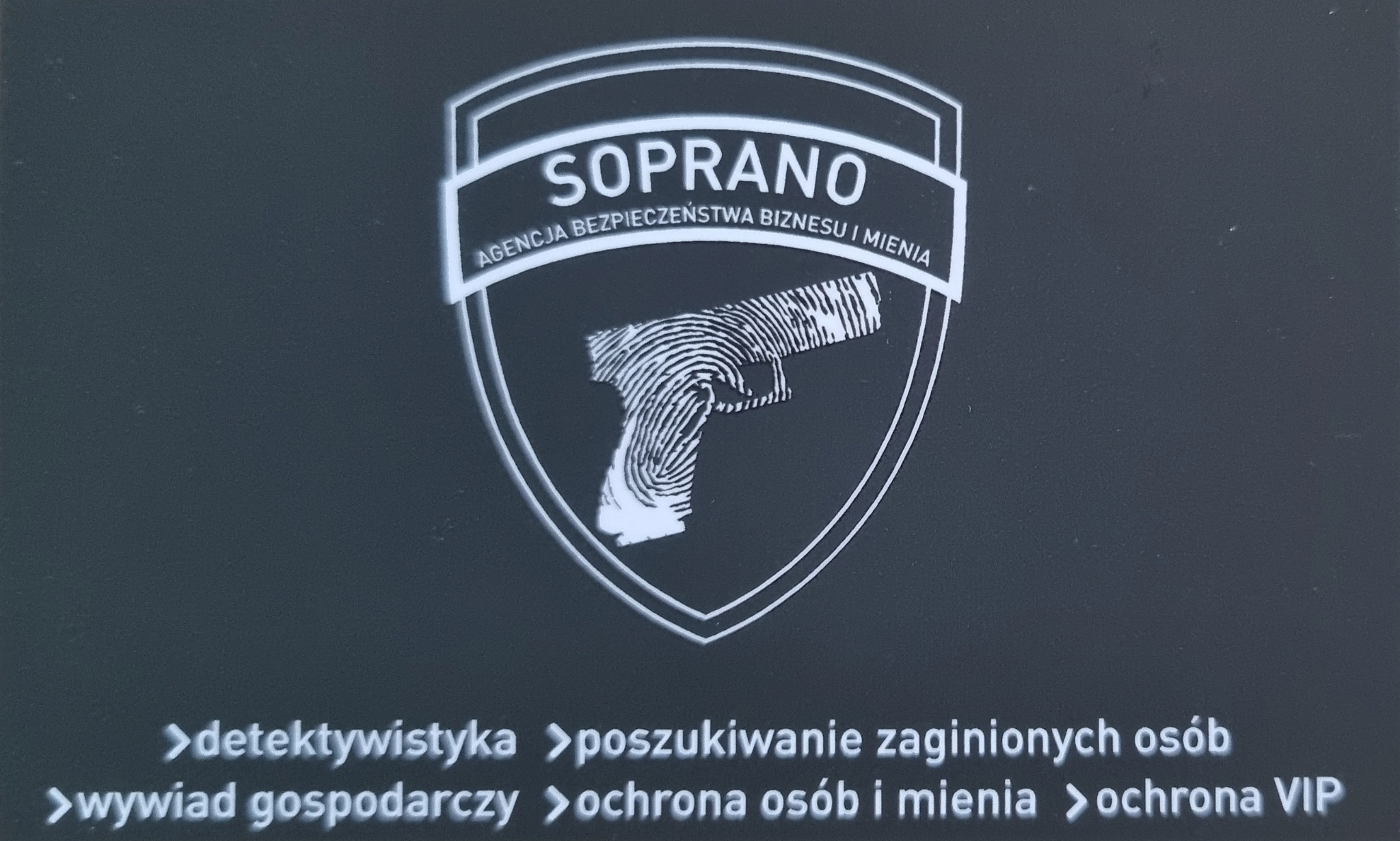 Logo firmy ochroniarskiej Soprano z motywem odcisku palca w kształcie pistoletu na ciemnym tle. Pod spodem wymienione usługi: detektywistyka, poszukiwanie zaginionych osób, wywiad gospodarczy...